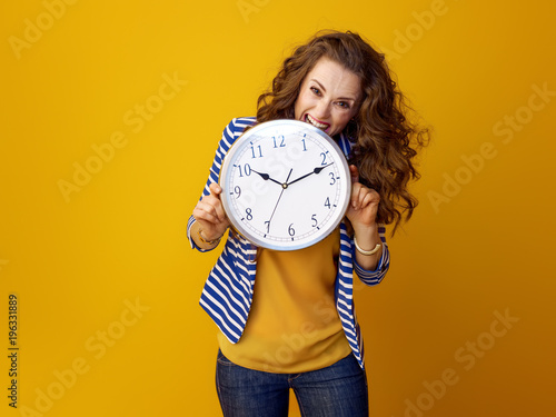 stressed stylish woman against yellow background biting clock