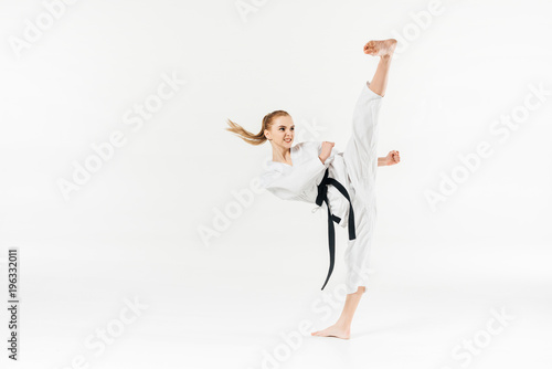 Female karate fighter with black belt performing kick isolated on white