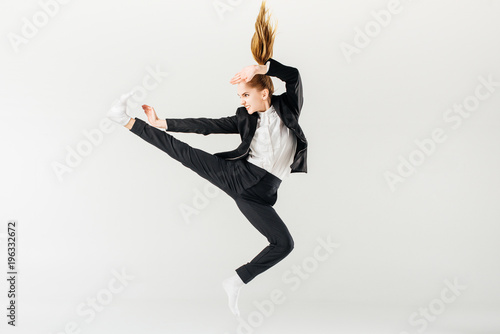 female karate fighter jumping and performing kick in suit isolated on grey