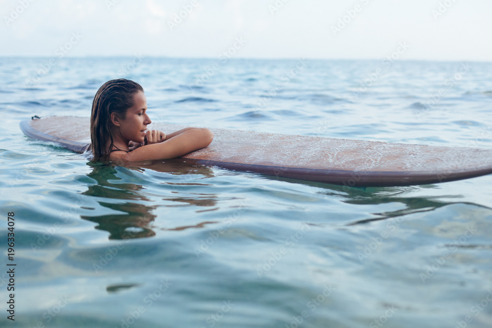 Joyful woman in have fun before surfing. Surfer girl hold surf board, look at sunset sky. People in sport adventure camp, extreme water activity on family summer beach vacation. Watersport background
