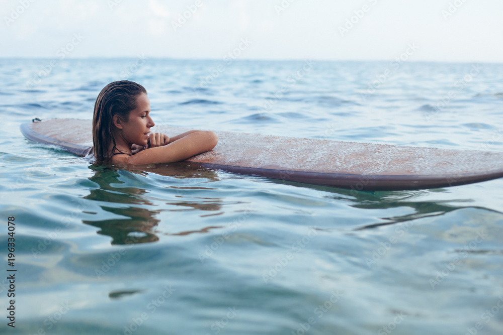 Joyful woman in have fun before surfing. Surfer girl hold surf board, look at sunset sky. People in sport adventure camp, extreme water activity on family summer beach vacation. Watersport background Joyful woman in have fun before surfing. Surfer girl hold surf board, look at sunset sky. People in sport adventure camp, extreme water activity on family summer beach vacation. Watersport background