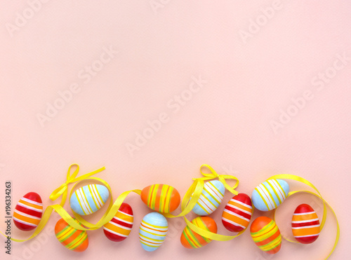Colorful easter eggs and ribbons on a pink background with empty space. Top view