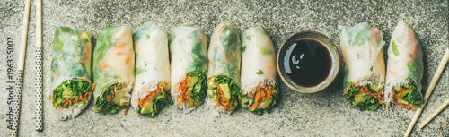 Helathy Asian cuisine. Flat-lay of vegan spring, summer rice paper rolls with vegetables, sauce, chopsticks over concrete background, top view, wide composition. Clean eating, dieting food