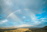 A rainbow over the plains of Namibia with a blue sky and rain clouds over the dry landscape