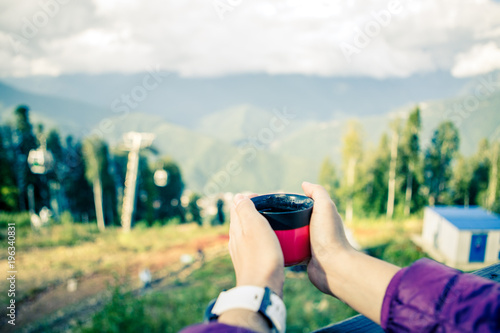 Photo of woman's hands with cup on blurred background of autumnal park