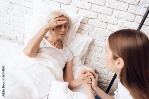 Girl is nursing elderly woman at home. They are holding hands. Woman is feeling bad.