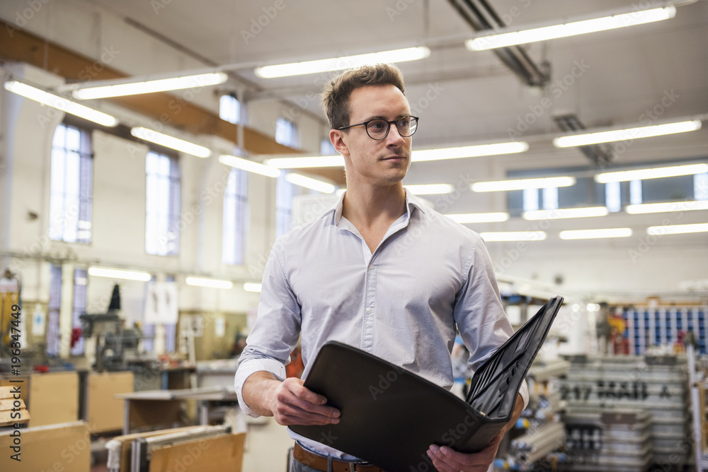 Young businessman in factory holding folder Young businessman in factory holding folder