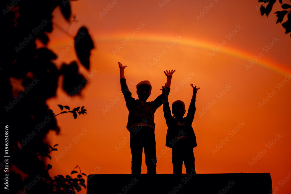 Two brothers with their hands up under the rainbow on sunset in summer. Two brothers with their hands up under the rainbow on sunset in summer.