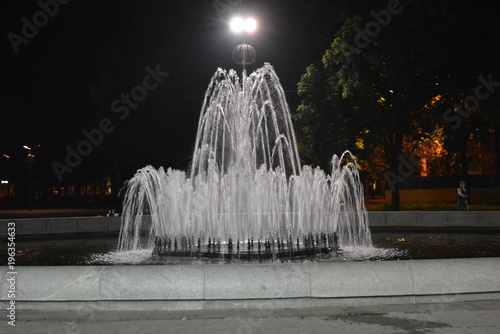 Nice night city, a fountain in the center of the park surrounded by lanterns