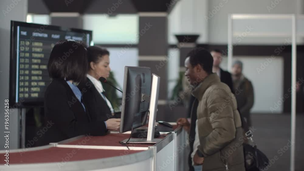 Two female airport security personnel checking identification at a check-in or boarding counter at the departure terminal holding the passports of two male passengers Two female airport security personnel checking identification at a check-in or boarding counter at the departure terminal holding the passports of two male passengers