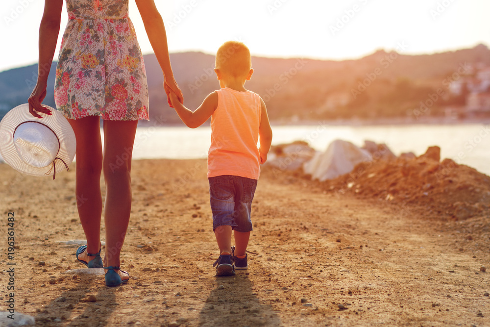 Rear view of mother walking with her son on dirt road by the sea.