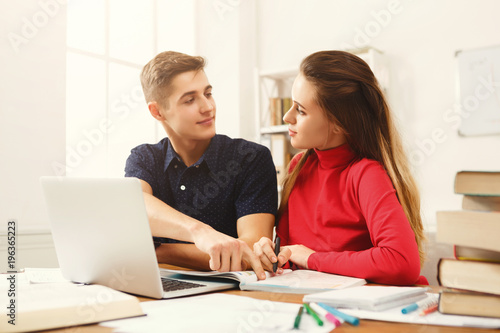 Male and female students at wooden table full of books