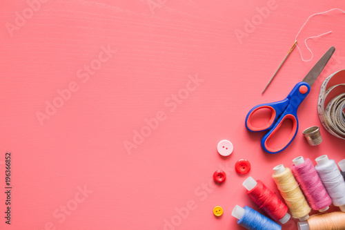 Colorful spools of threads with sewing tools on the pastel pink background. Mock up for dressmakers or textile shops offers as advertising or other ideas. Womanly hobby. Empty place for text.