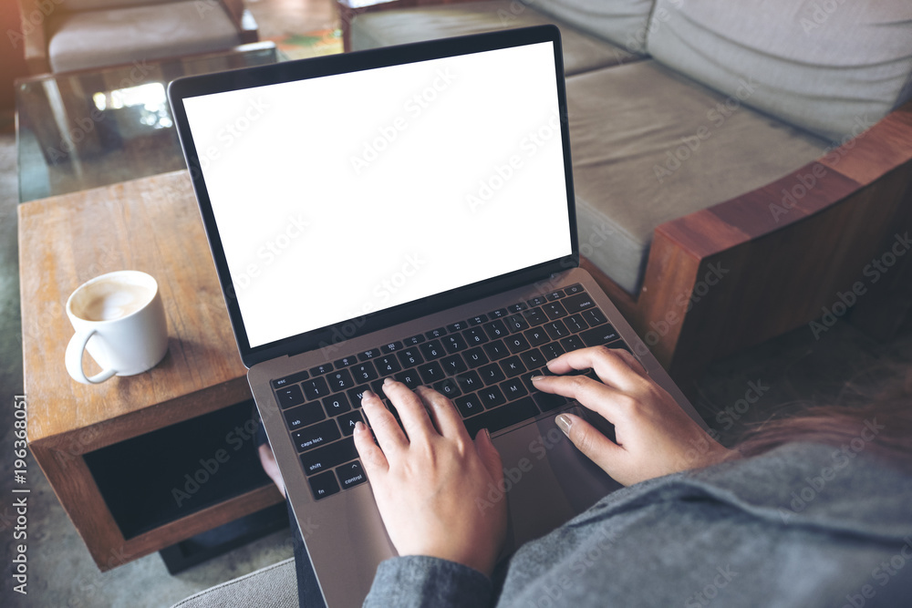 Mockup image of business woman using and typing on laptop with blank white desktop screen and coffee cup on wooden table in cafe Mockup image of business woman using and typing on laptop with blank white desktop screen and coffee cup on wooden table in cafe
