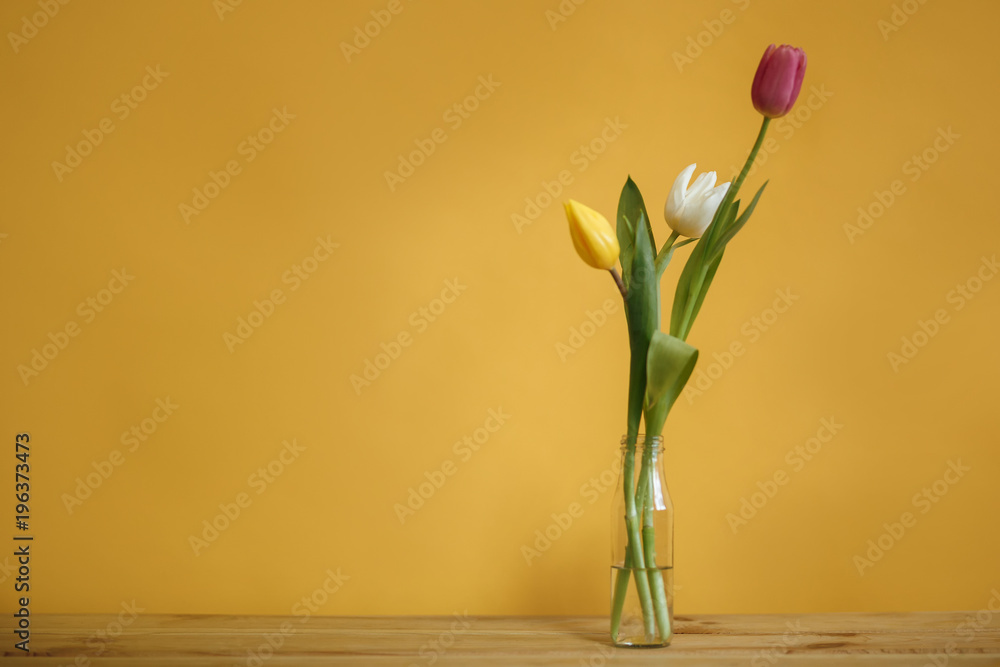 composition of three tulips in a bottle against a yellow wall background composition of three tulips in a bottle against a yellow wall background