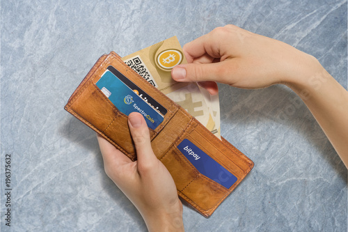 Portafoglio aperto con bitcoin cartacei e carte di credito virtuali, sfondo pietra