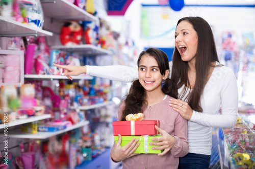 Woman and smiling daughter with gifts standing in the toys shop