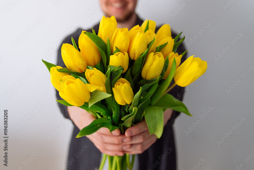 Fototapeta premium man holds bouquet of yellow tulips in front of him. romantic gift for woman. white background