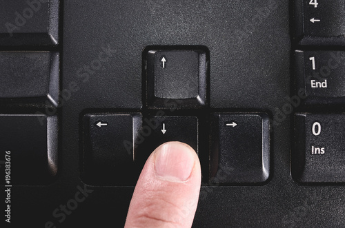 Fotografija Human finger pressing the directional down key from a black keyboard