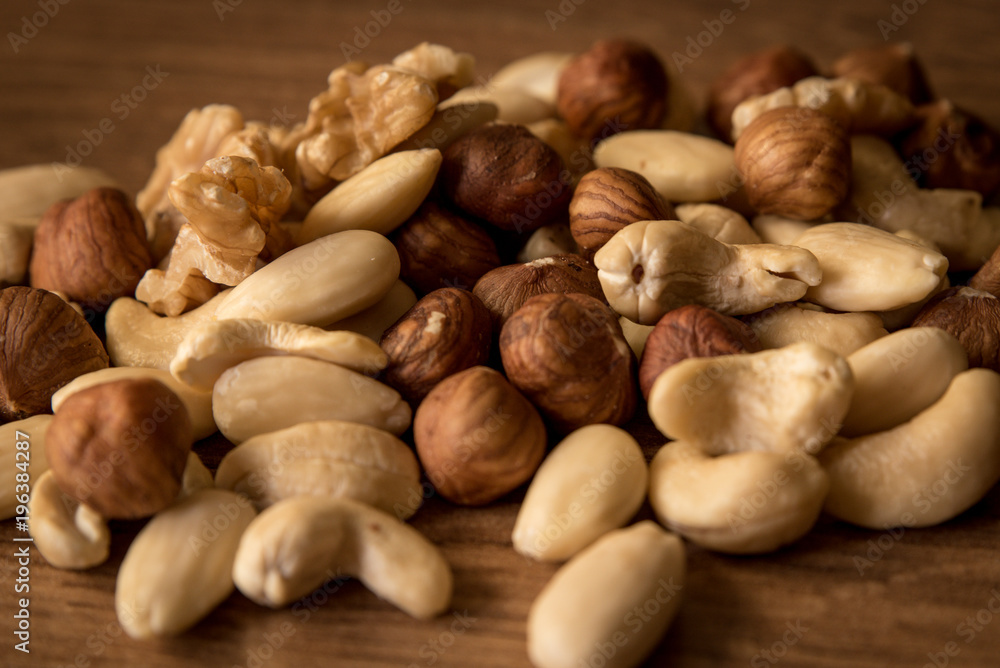 nuts, in a white bowl, fried on a dark wood background, mixture of walnuts, almonds and roasted nuts, top view