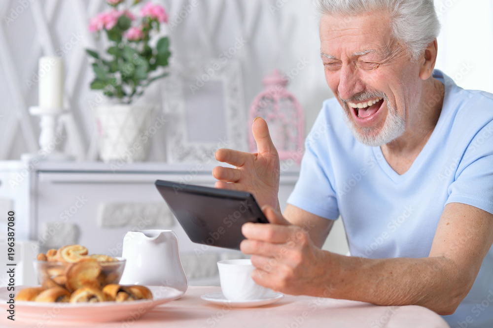 senior man using tablet while drinking tea senior man using tablet while drinking tea