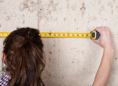 Young woman working with measuring tape in house under reconstruction photo