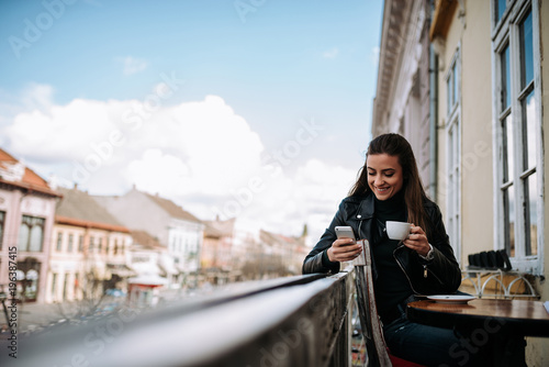  Enjoying cup of coffee and using phone on the balcony at old city core.