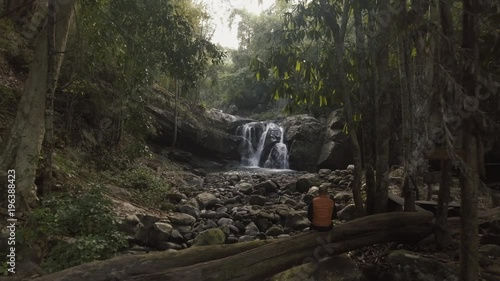 aerial shot man sitting on death tree in front of waterfall in tropical forest at early morning slow camera movement