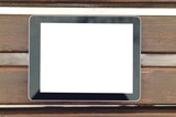 Tablet computer with blank isolated screen is laying on wooden background of bench in the park.