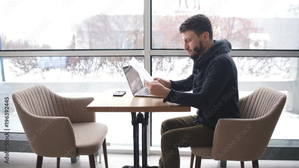 a young businessman talking on the phone and working at a laptop in a cafe a young businessman talking on the phone and working at a laptop in a cafe