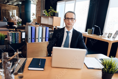 Adult confident man in suit is sitting at table in office. Lawyer is at work.