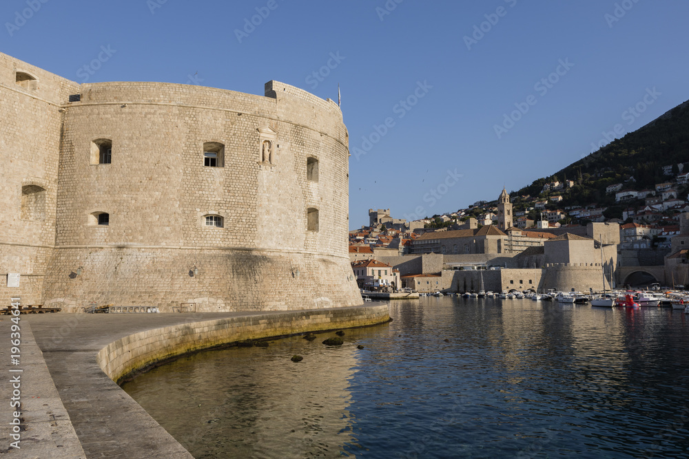 The mighty city wall of Dubrovnik in the morning light and in the background the boat harbor