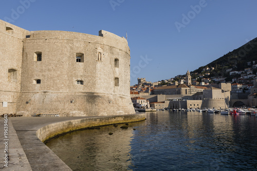The mighty city wall of Dubrovnik in the morning light and in the background the boat harbor