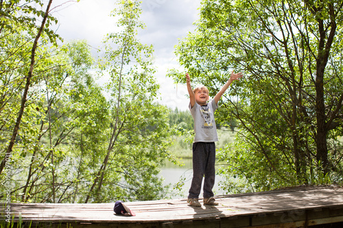 Boy throws leaves from a bridge at summer.