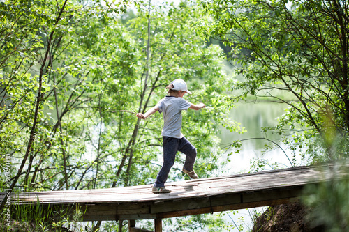 A boy is going for a trip on a a bridge in a forest near a lake. Funny and happy childhood.