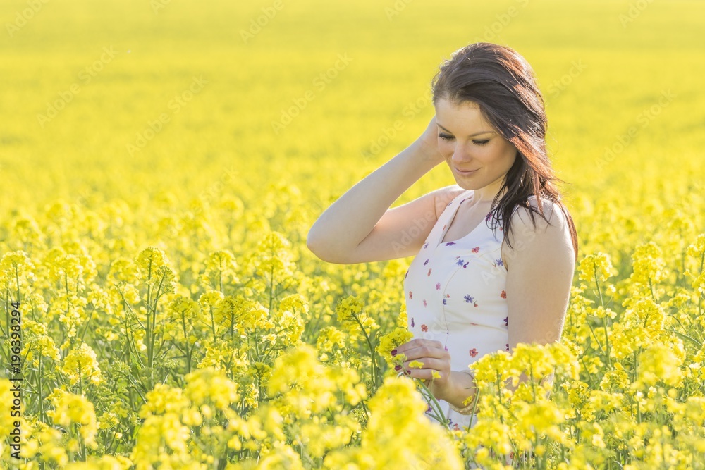 Beatiful youth woman with flower in summer meadow looking down. Beautiful girl eyes closed in yellow flowers field infinite horizon. Sunny sun sunshine and authentic lifestyle in windy weather hair Beatiful youth woman with flower in summer meadow looking down. Beautiful girl eyes closed in yellow flowers field infinite horizon. Sunny sun sunshine and authentic lifestyle in windy weather hair