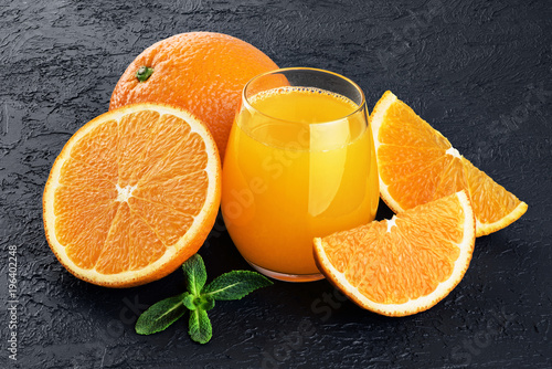Glass with orange juice, oranges and mint on a dark background.