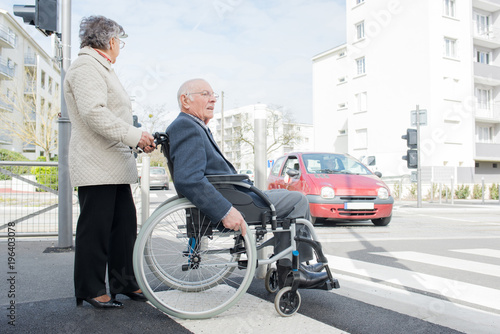 wife and elderly person in a wheelchair crossing the road