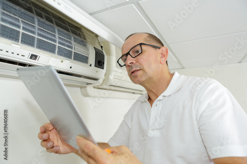 senior technician with tablet by air conditioning unit