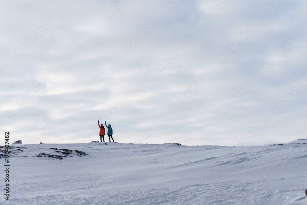 Two young girls in bright jackets travel on snowy peaks of the tundra in winter in a frost drowning in the snow