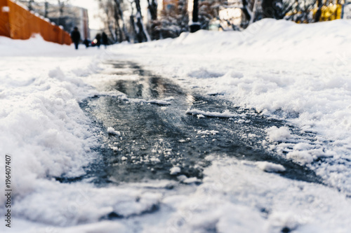 Slippery shiny ice on the sidewalk in winter under the snow beckons to ride on it to enjoy