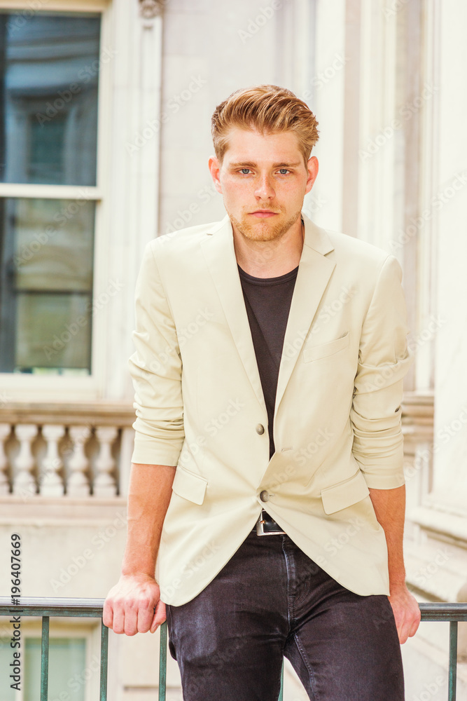 Young American Businessman with little beard, wearing beige blazer, black undershirt, sitting by railing in vintage office building in New York, tired, taking work break, thinking..