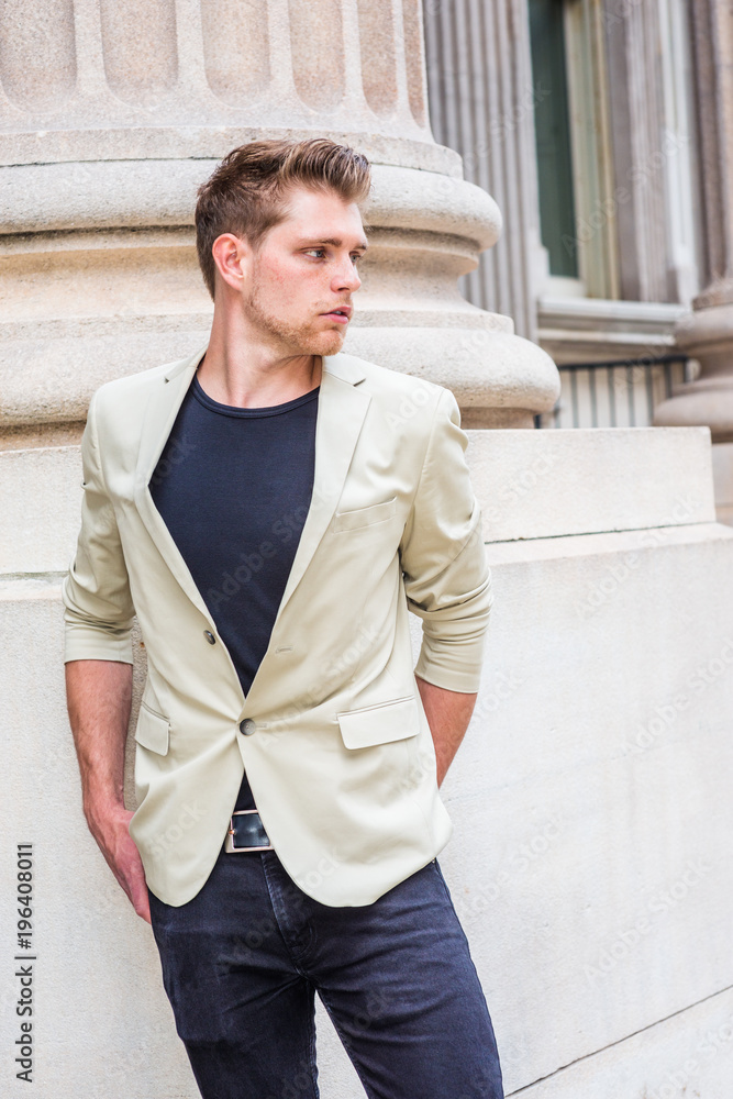 Young American Businessman with little beard, wearing beige blazer, black undershirt, pants, standing by column outside vintage office building, taking work break, thinking.. Young American Businessman with little beard, wearing beige blazer, black undershirt, pants, standing by column outside vintage office building, taking work break, thinking..