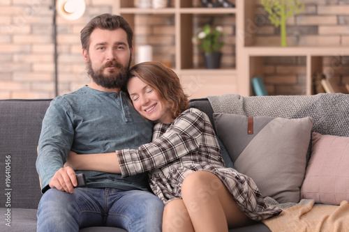 Happy couple watching TV while sitting on sofa at home