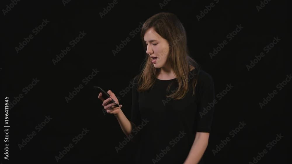 A beautiful young lady showing I am happy gesture and using a phone against a black background. Medium Shot A beautiful young lady showing I am happy gesture and using a phone against a black background. Medium Shot