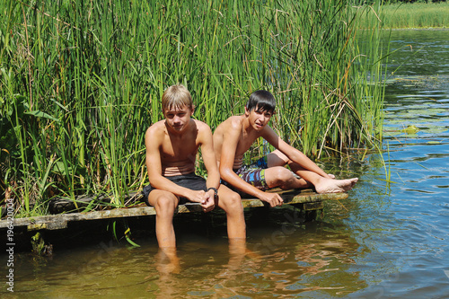 Two boys, a teenager rest on the river bank, on a hot day