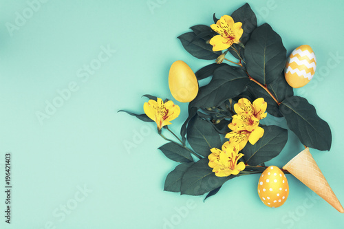 Happy Easter concept. Bouquet of green leaf with yellow spring s flowers and colorful easter eggs on blue background