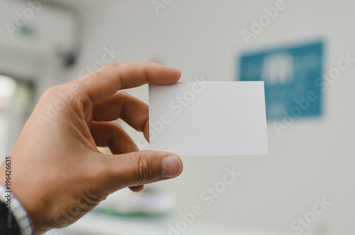 Closeup on hand of a person holding showing white business card over blurry office background