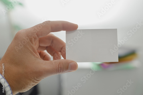 Closeup on hand of a person holding showing white business card over blurry office background