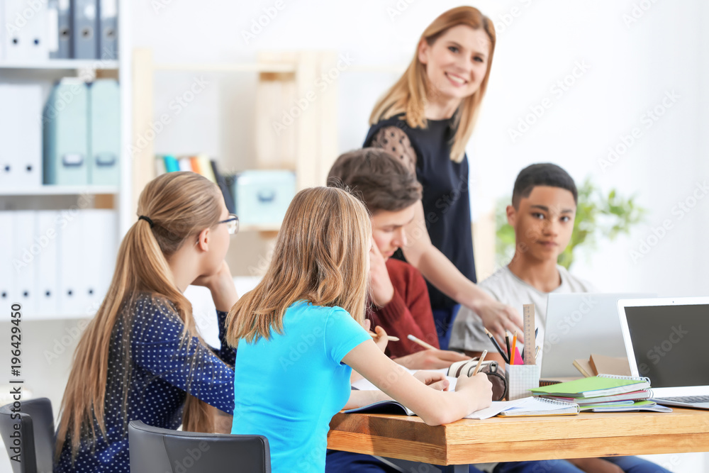 Obraz premium Group of teenagers doing homework with teacher in classroom